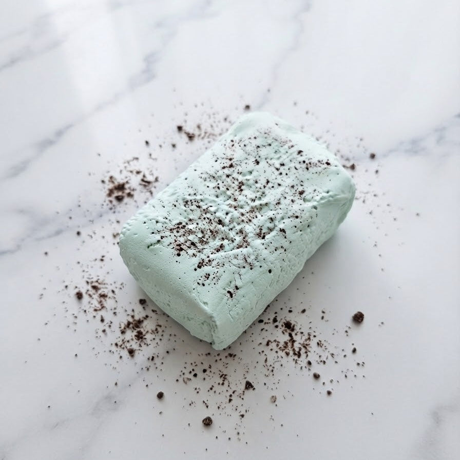 A rectangular mint green pastry or dessert piece with dark cookie crumbles sprinkled on top, resting on a white marble surface with scattered crumbs.