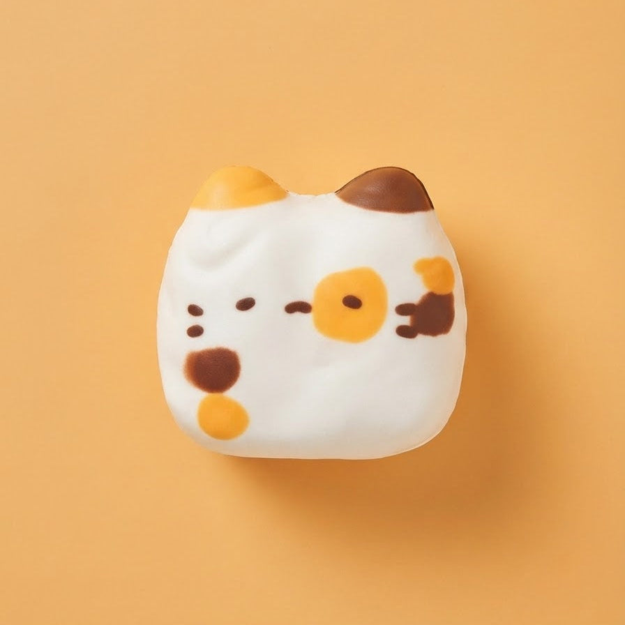 A white cat-shaped squishy toy with orange, brown, and black facial details, centered on a solid orange background.