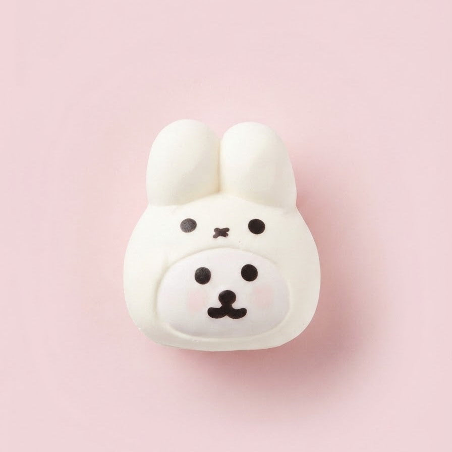 A white bunny-shaped wall hook with black facial features, shown against a solid light pink background.