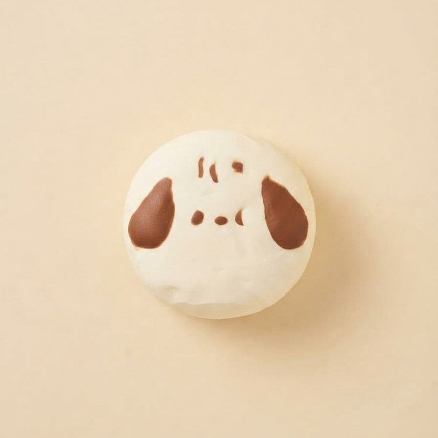 A round white macaron with a simple brown face design, centered on a solid beige background.