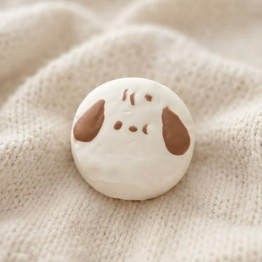 A small round white button with a brown cartoon dog face, resting on a soft beige knitted fabric background.