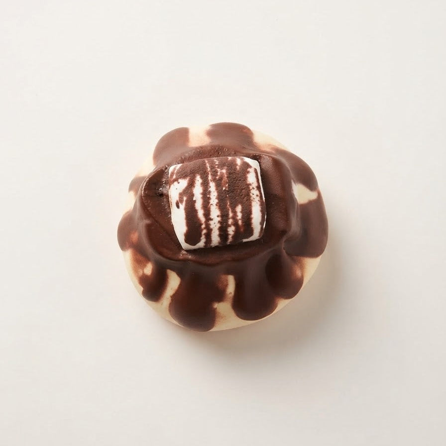 A single chocolate-covered pastry or dessert piece with dark chocolate drizzle and a white striped center, photographed from above on a plain light background.