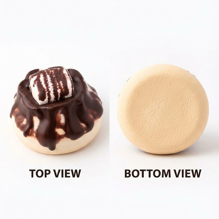 A two-view product shot on a white background showing a round beige item from the top and bottom. The top view shows the item decorated with dark brown chocolate drizzle and a white marshmallow topper, while the bottom view shows the plain beige underside.