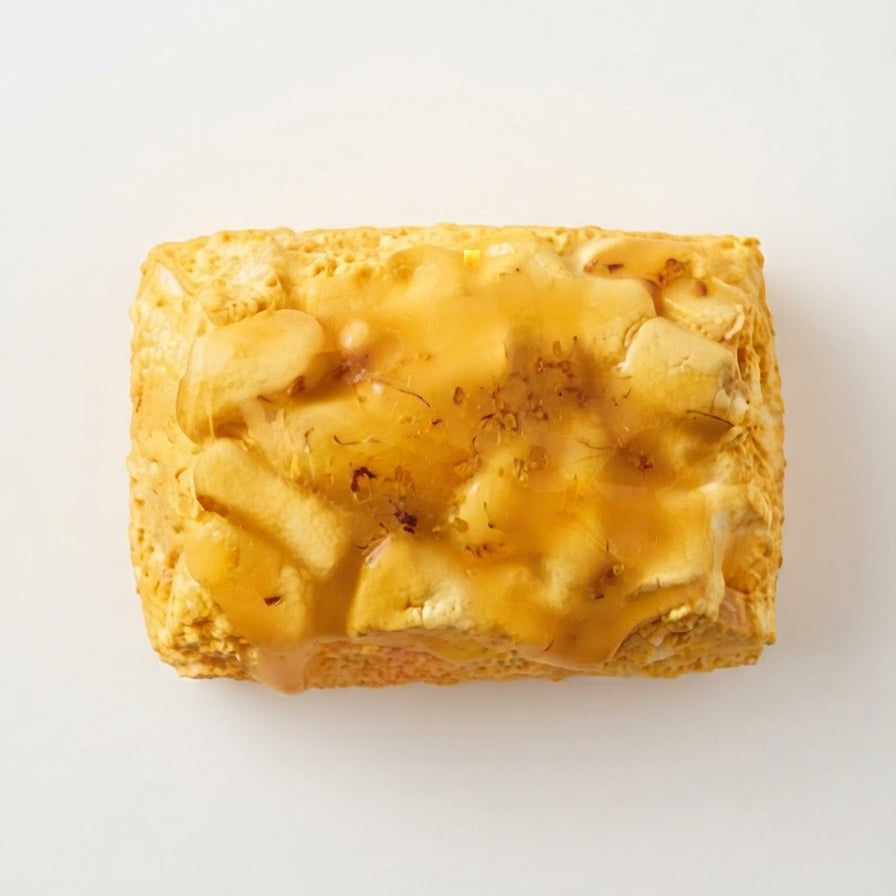 A rectangular pastry or bread slice topped with glossy golden caramel and sliced bananas, photographed from above on a plain white background.