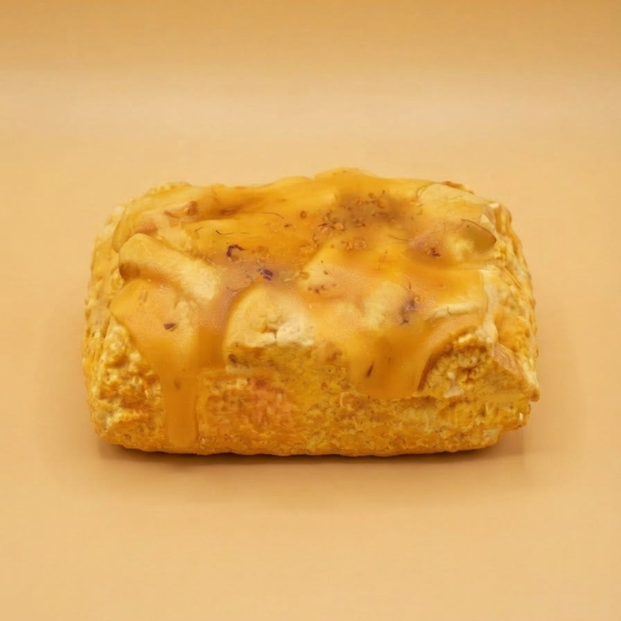 A rectangular golden-brown pastry or bread loaf topped with glossy amber glaze, centered on a warm beige studio background.