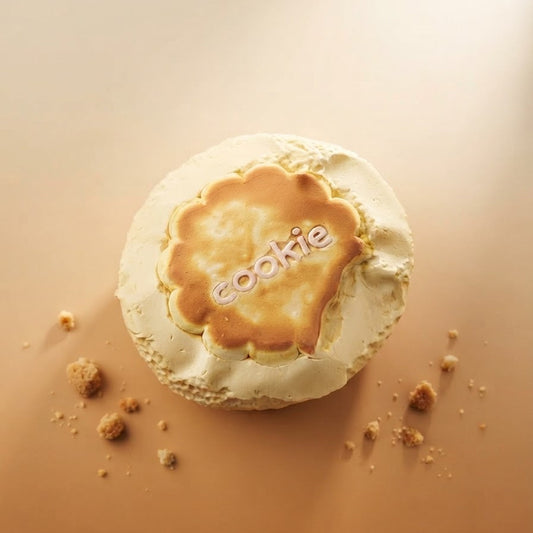 A round meringue-based dessert topped with a golden-brown caramelized center, photographed from above on a warm beige surface with a few crumbs nearby. The word 'cookie' is printed across the center.