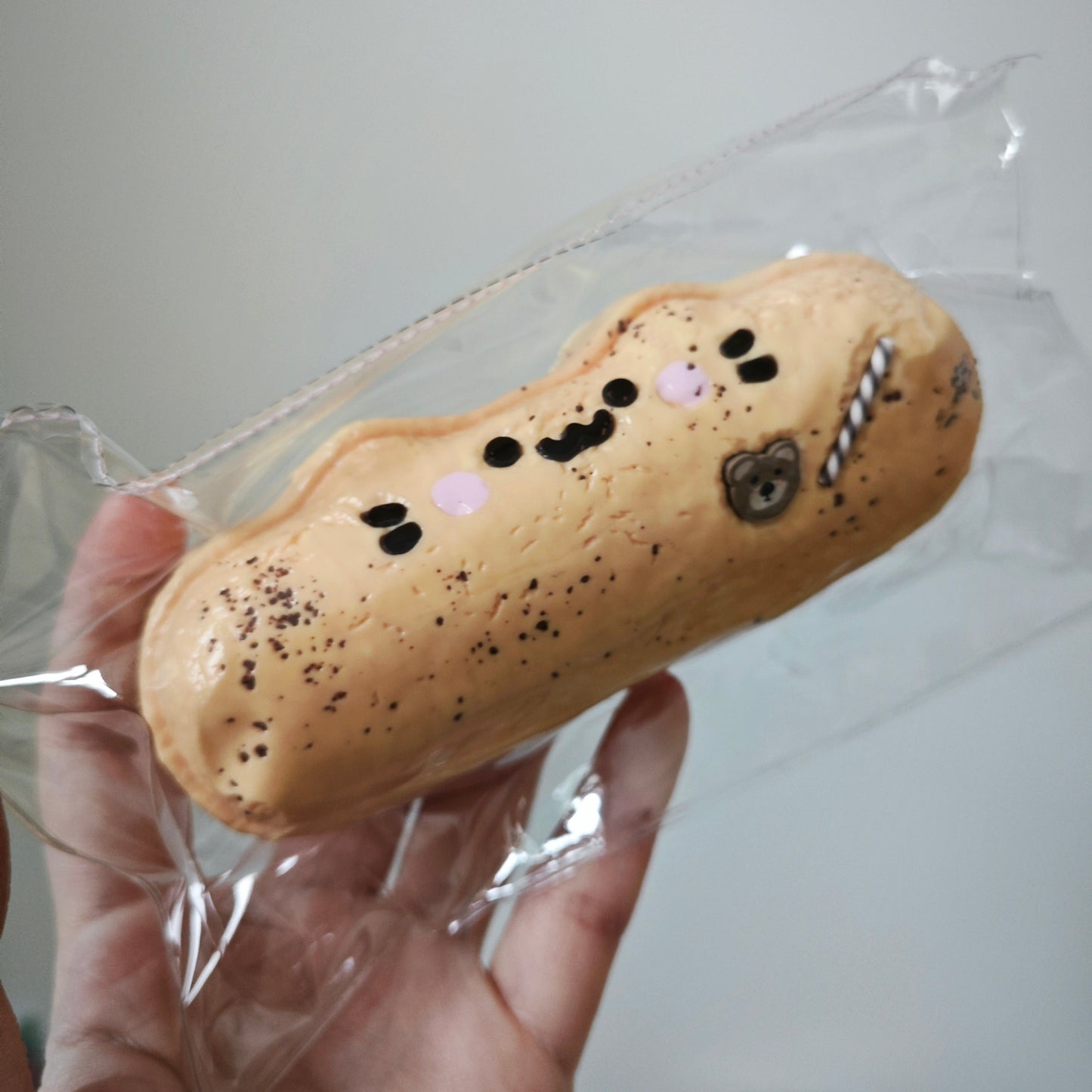 A hand holding a packaged novelty item shaped like a peanut with a cute cartoon face, wrapped in clear plastic against a plain light background.