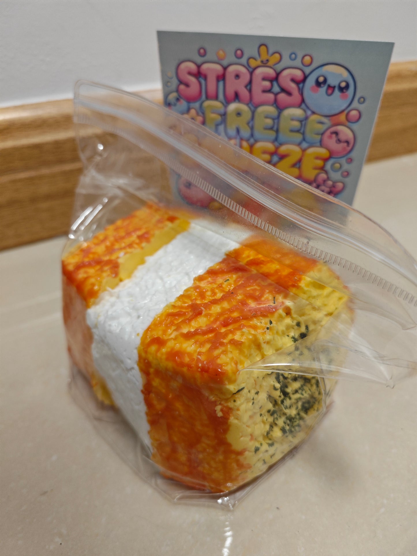 A packaged novelty stress toy shaped like a slice of toast or sandwich bread, sealed in a clear plastic bag with a small card behind it that reads 'STRESS FREE ZUBE'.