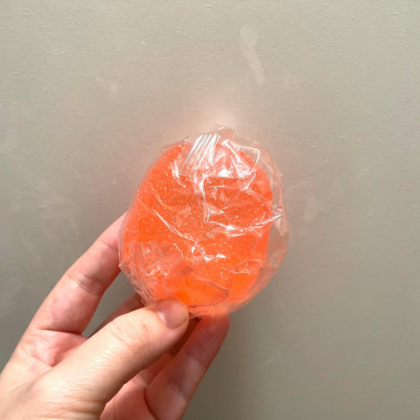 Hand holding a wrapped orange candy against a plain background