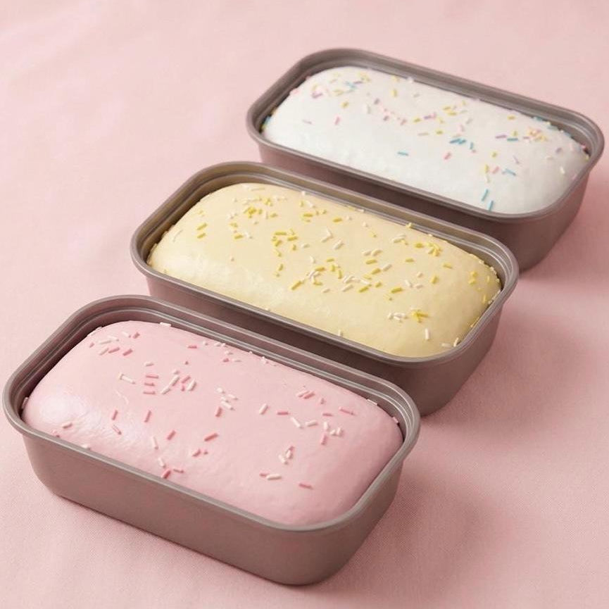 Three loaf pans with different colored ice cream on a pink background