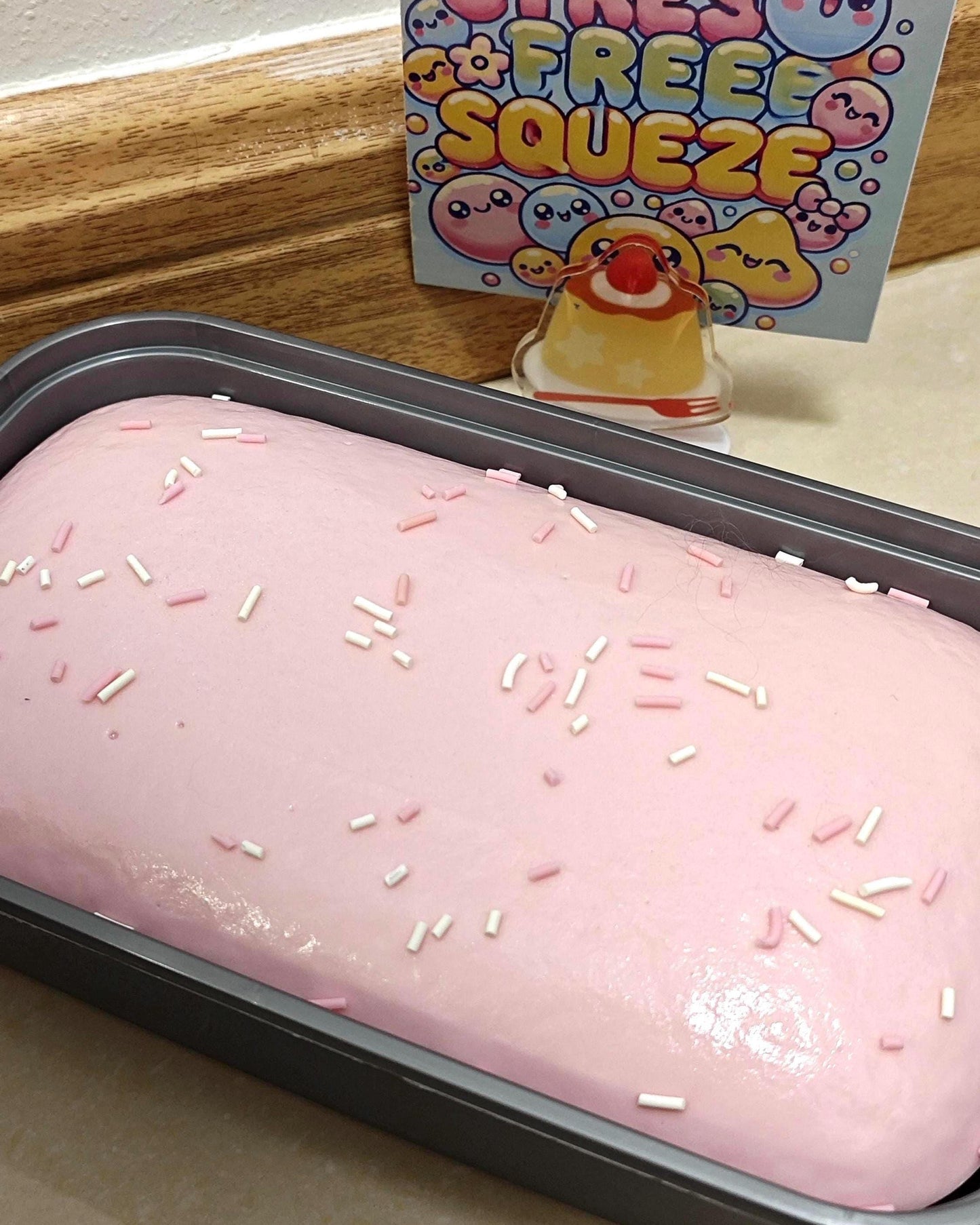 Pink frosted cake with sprinkles in a pan, with a 'Free Squeeze' toy in the background.