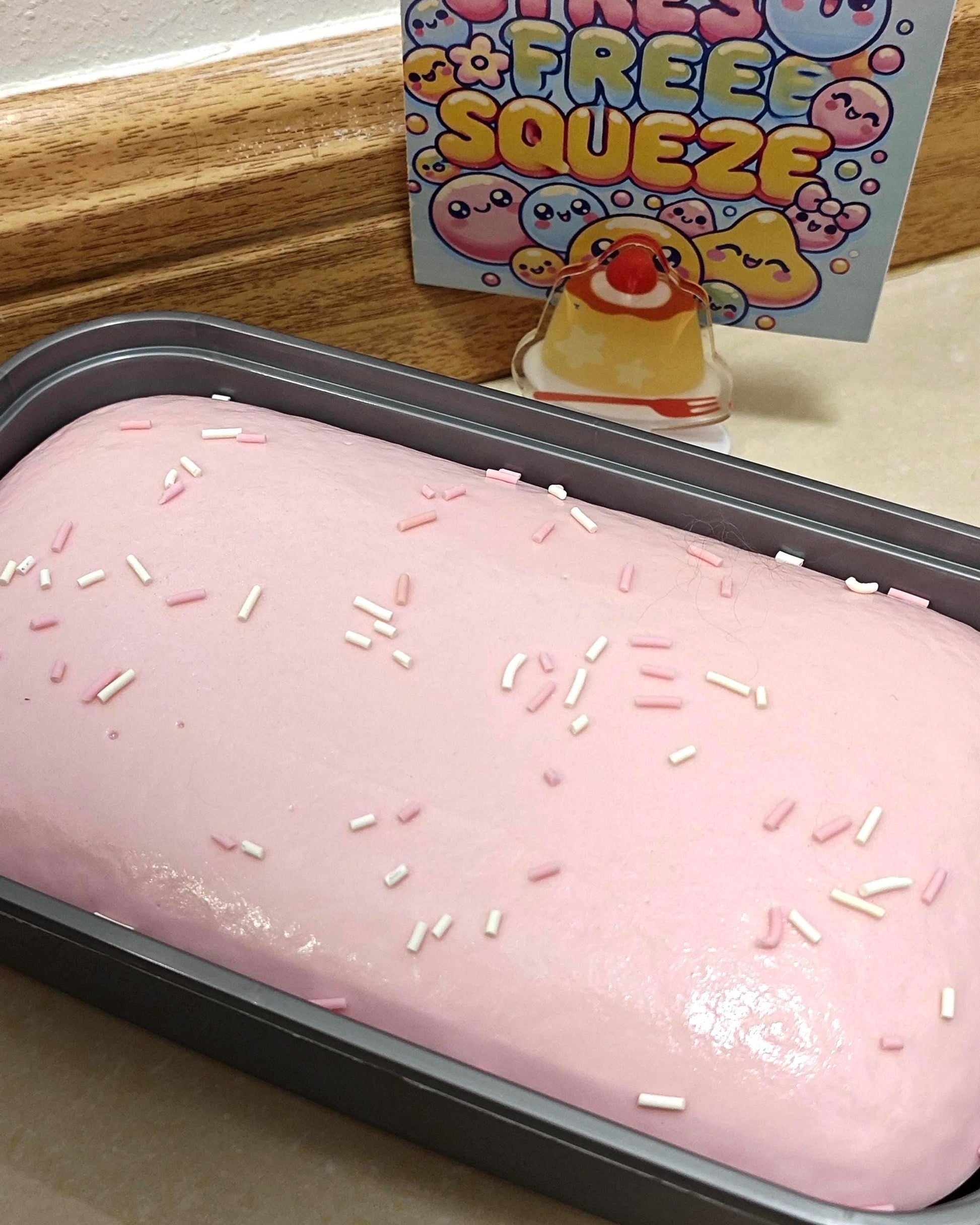 Pink frosted cake with sprinkles in a pan, with a 'Free Squeeze' toy in the background.