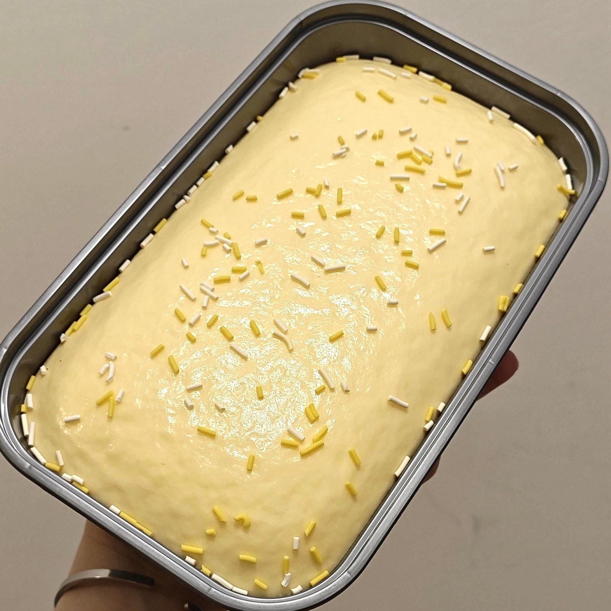 Baked cake with sprinkles in a metal loaf pan held by a person.