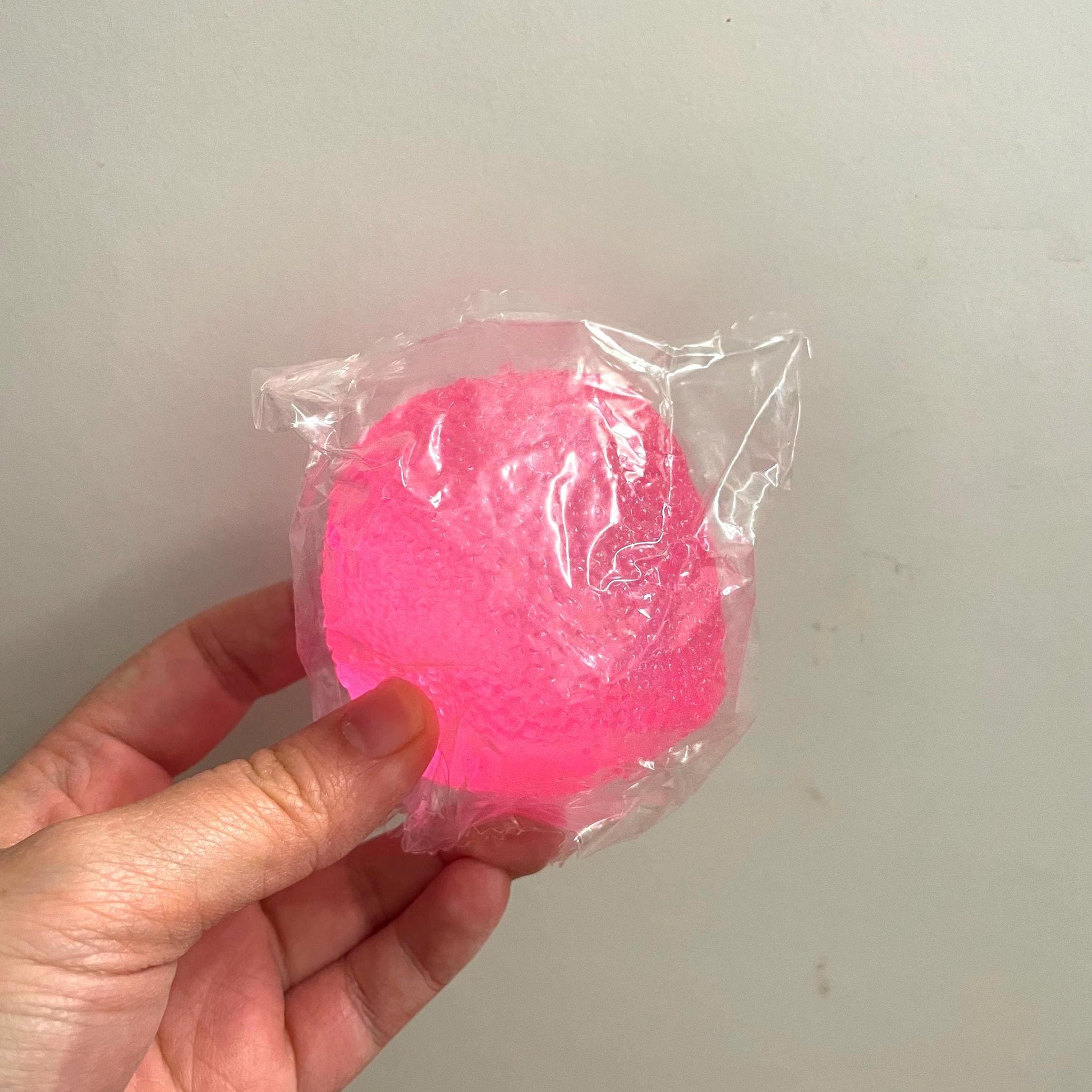 Pink object in clear plastic packaging held by a hand against a plain background