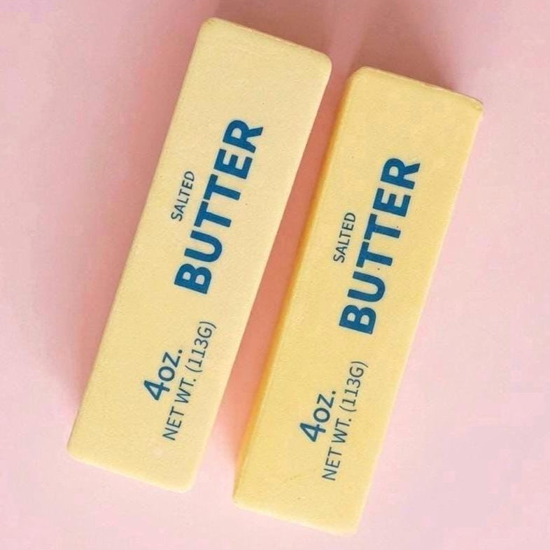 Two yellow butter sticks labeled 'SALTED BUTTER 4oz' on a soft pink background.