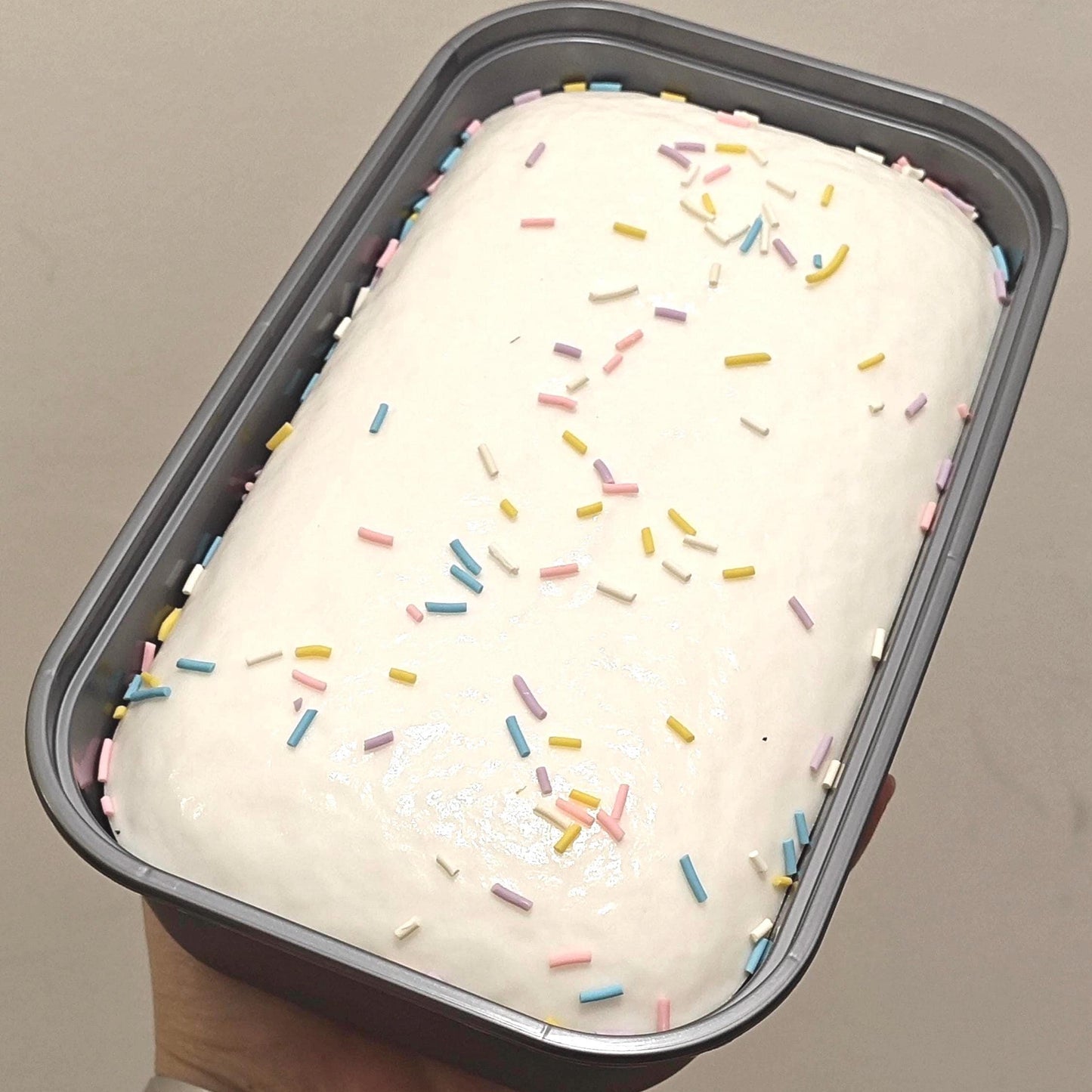 Loaf of bread with white icing and colorful sprinkles in a baking pan.