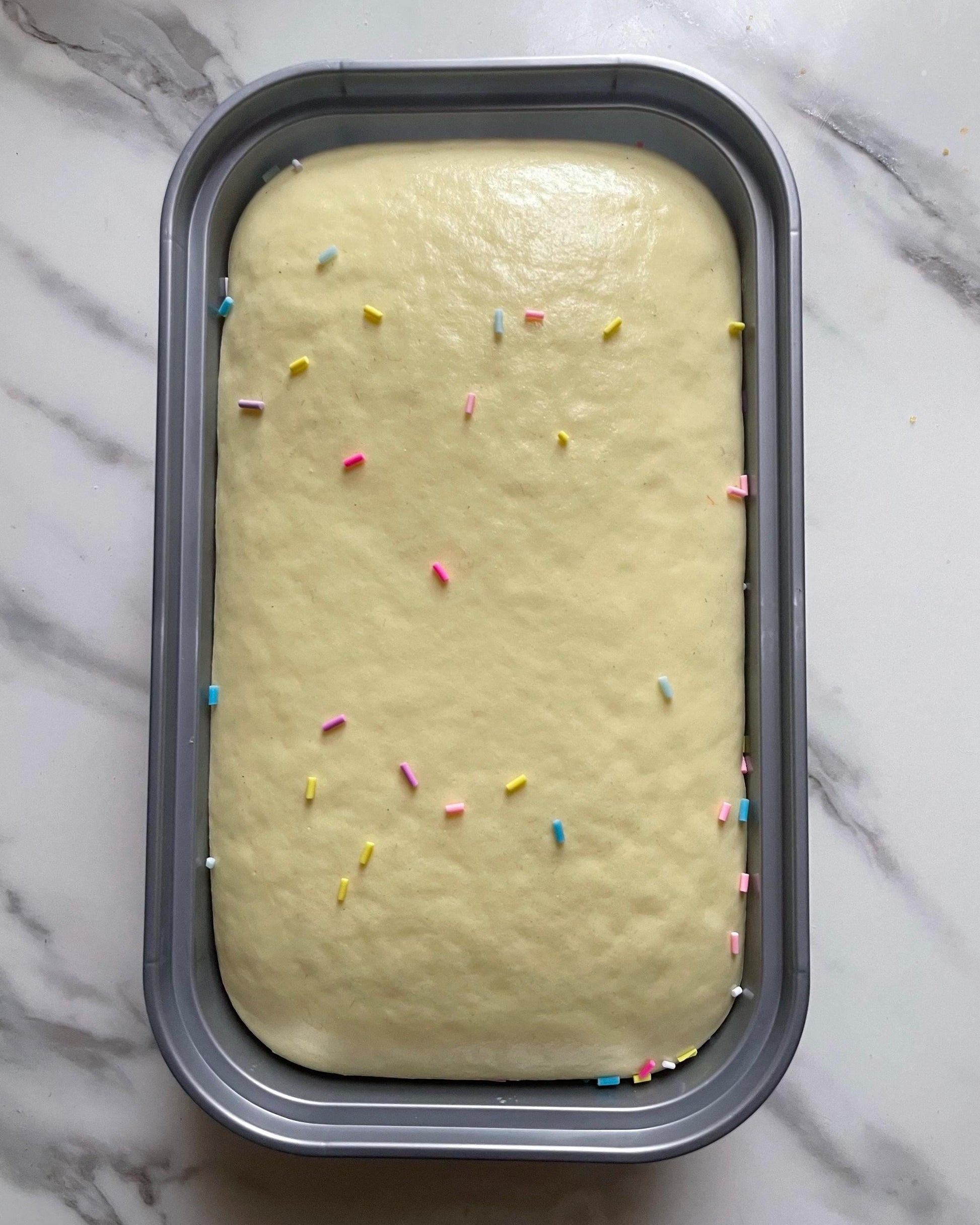 Unbaked cake batter with sprinkles in a loaf pan on a marble surface