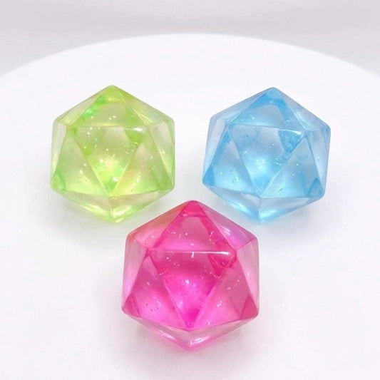 May include: Three faceted, gem-like objects in shades of green, blue, and pink. The objects have a geometric design and appear translucent, with a slight sparkle. The objects are arranged on a white surface.