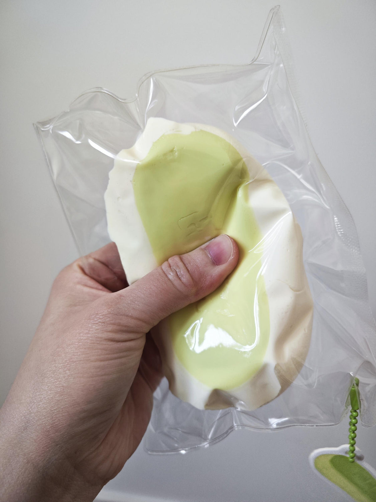 A hand holding a clear plastic bag containing a pale yellow and off-white textured item, shown against a plain light background.