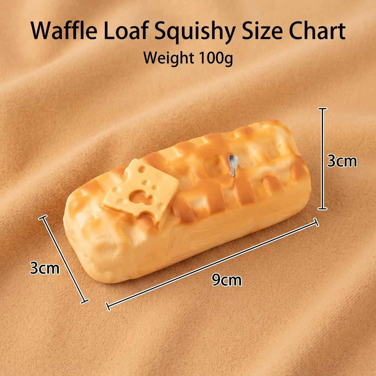 A waffle loaf-shaped squishy toy with a cheese detail, shown on a beige fabric background with overlaid dimension lines and text reading 'Waffle Loaf Squishy Size Chart' and 'Weight 100g'.
